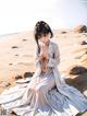 A woman in a white dress sitting on a sandy beach.